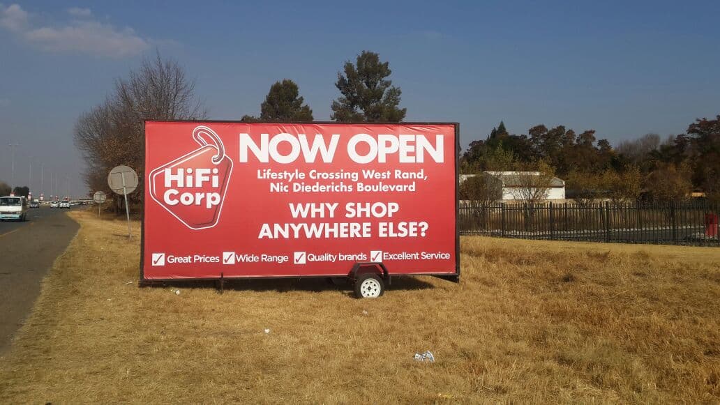 HiFi Corp store opening billboard on a Simply Visible trailer beside a West Rand main road
