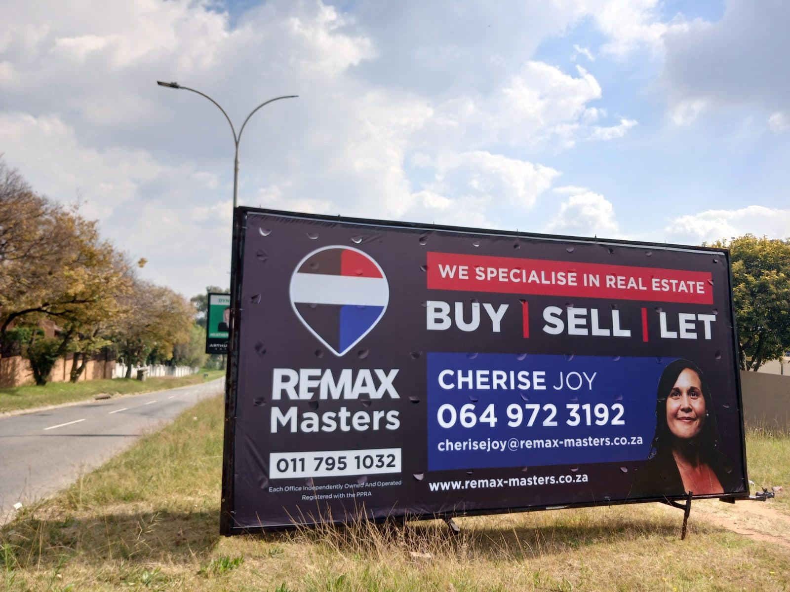 RE/MAX Masters agent billboard on a Simply Visible trailer parked on the verge of a suburban road